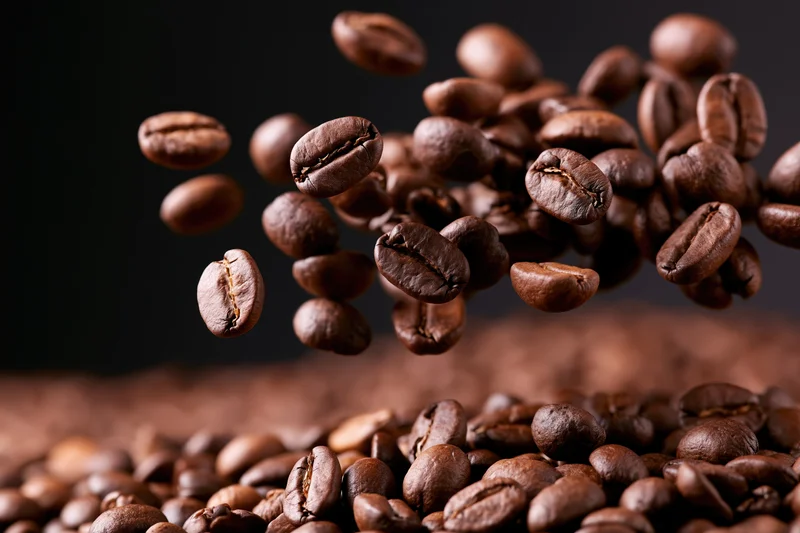 Roasted coffee beans falling and tumbling onto a pile against a dark background