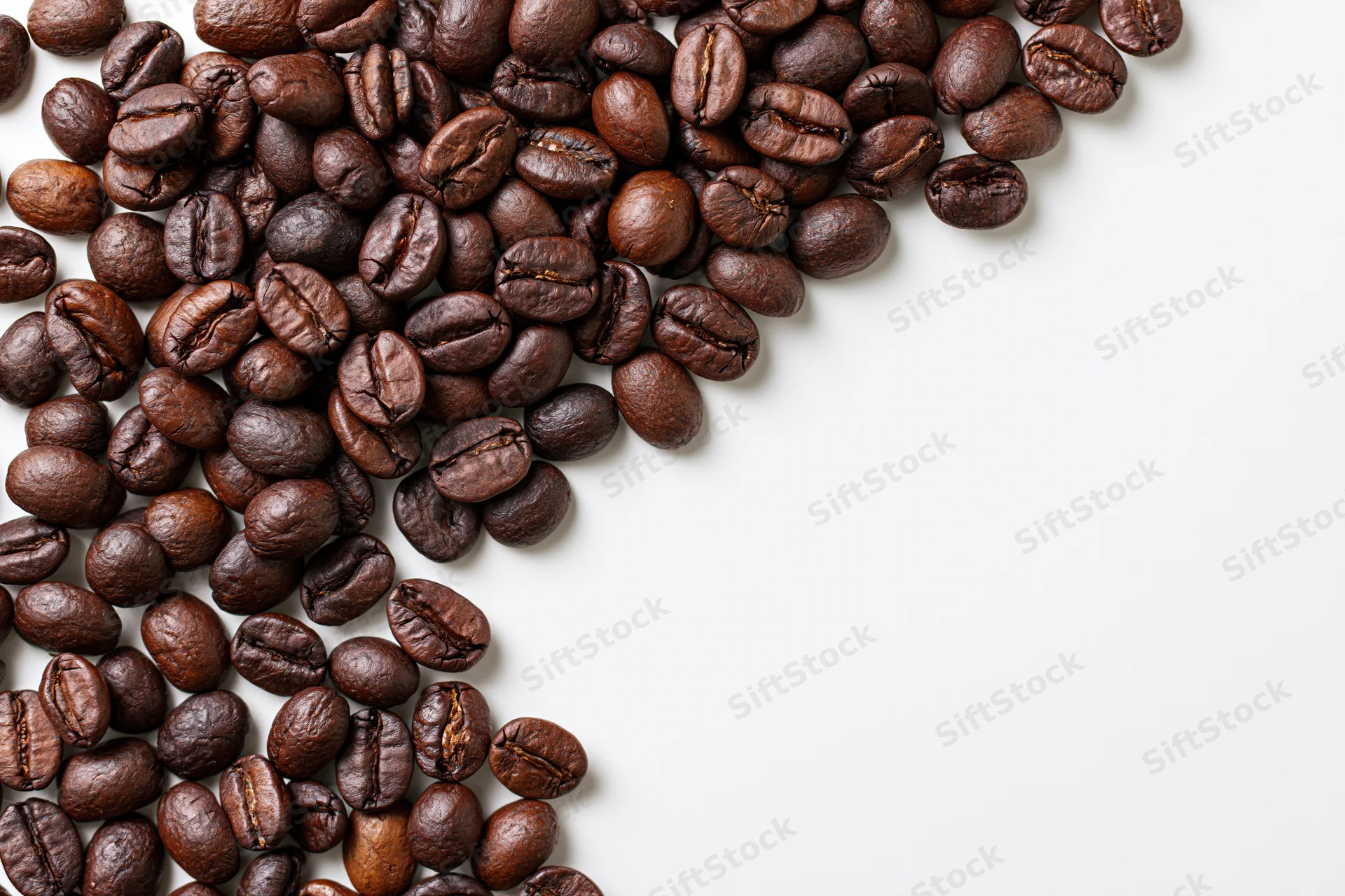 Roasted coffee beans scattered in upper left corner on white background with copyspace