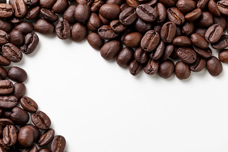 Roasted coffee beans scattered along the top and left edges on a white surface, leaving copyspace in the center
