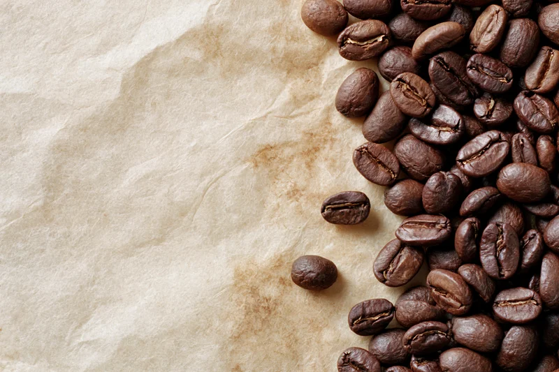 Roasted coffee beans scattered along the right edge of crumpled parchment paper