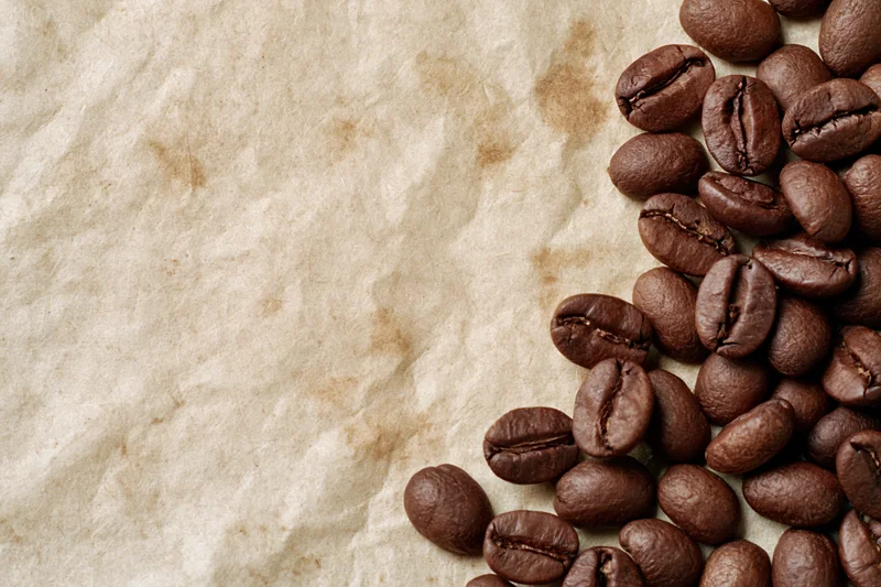 Roasted coffee beans scattered along the right edge of crumpled parchment paper