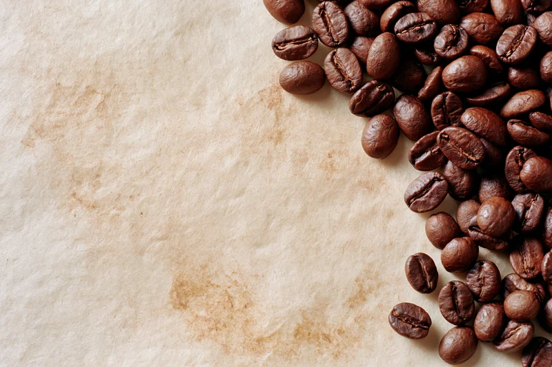 Roasted coffee beans scattered along the right edge of aged parchment paper
