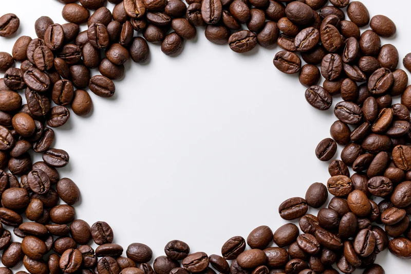 Roasted coffee beans arranged in a curved border on a white background with copyspace