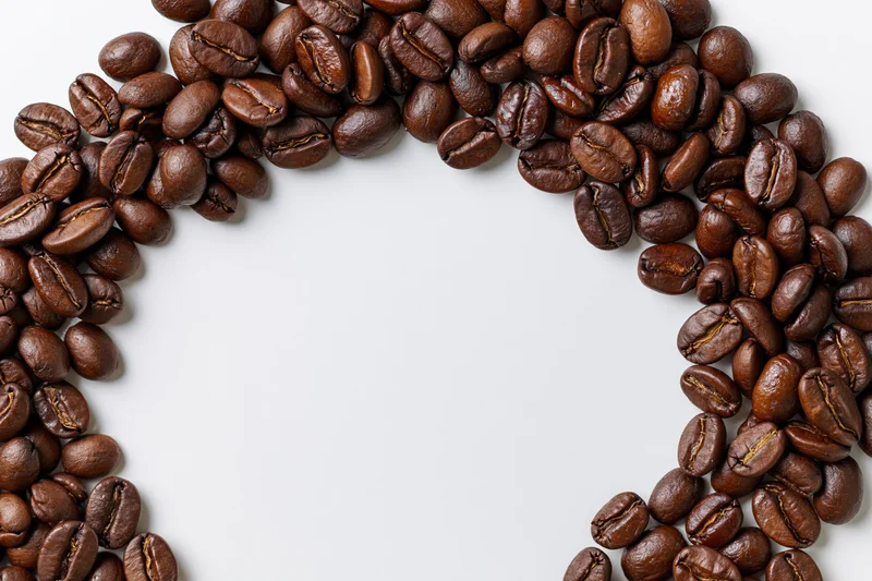 Roasted coffee beans arranged in a curved border on a white surface with copyspace