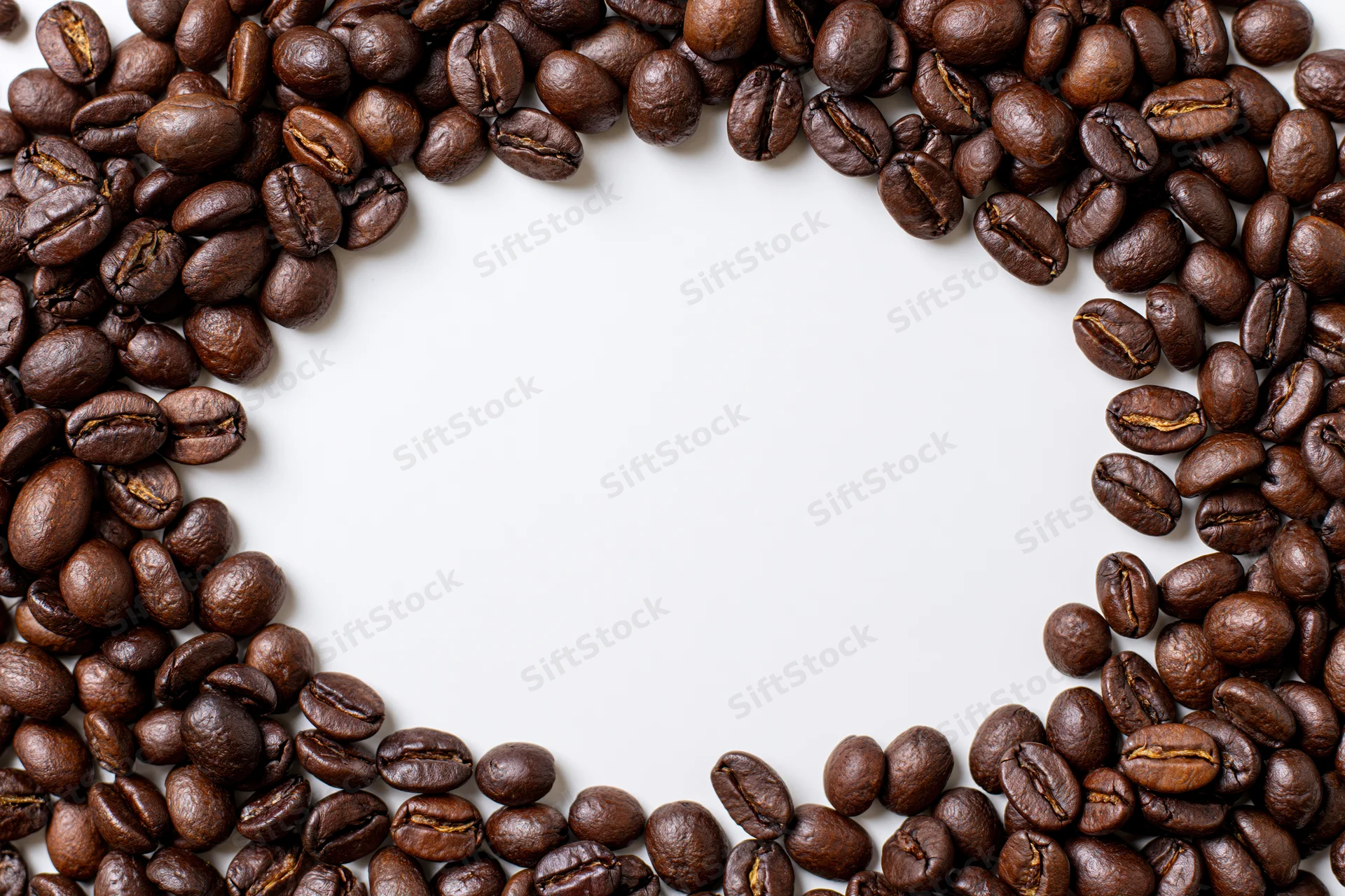 Roasted coffee beans arranged in a curved border on white background with copyspace