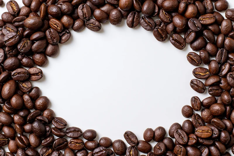 Roasted coffee beans arranged in a curved border on white background with copyspace