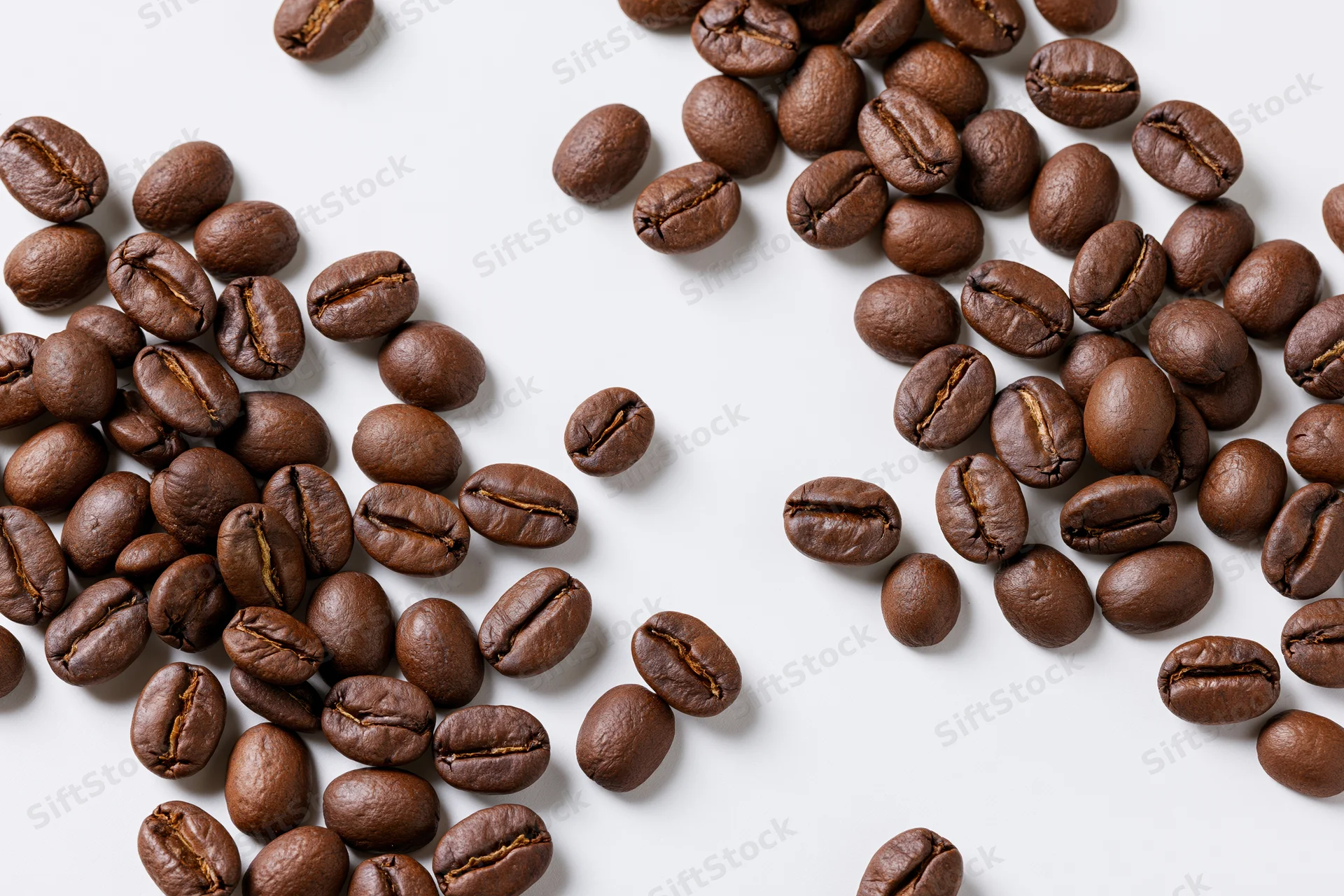 Roasted coffee beans scattered across a flat white surface in a top-down view