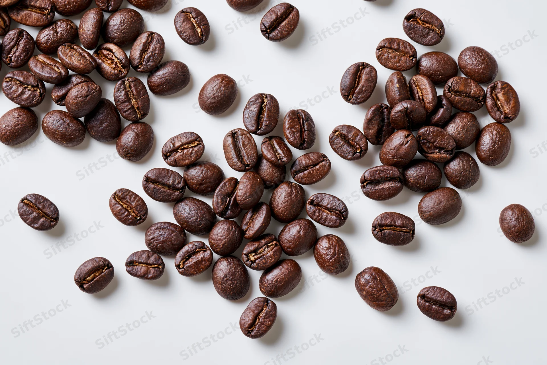 Roasted coffee beans scattered across a flat white surface in a top-down view