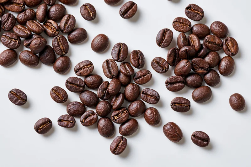 Roasted coffee beans scattered across a flat white surface in a top-down view