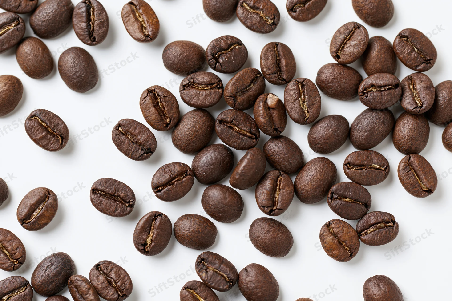 Roasted coffee beans scattered across a white surface in a flat lay top view