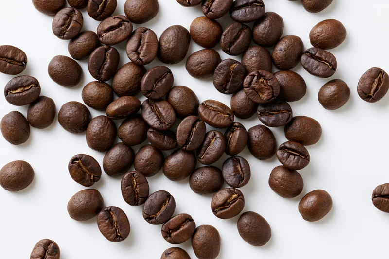 Roasted coffee beans scattered across a flat white surface