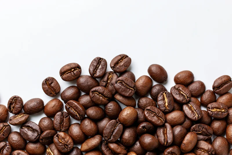 Roasted coffee beans scattered along the bottom left on a white background