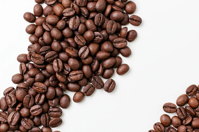 Roasted coffee beans scattered loosely along the bottom-left on white background
