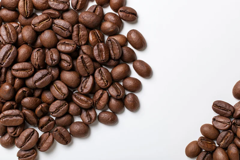 Roasted coffee beans scattered loosely on white background with copyspace