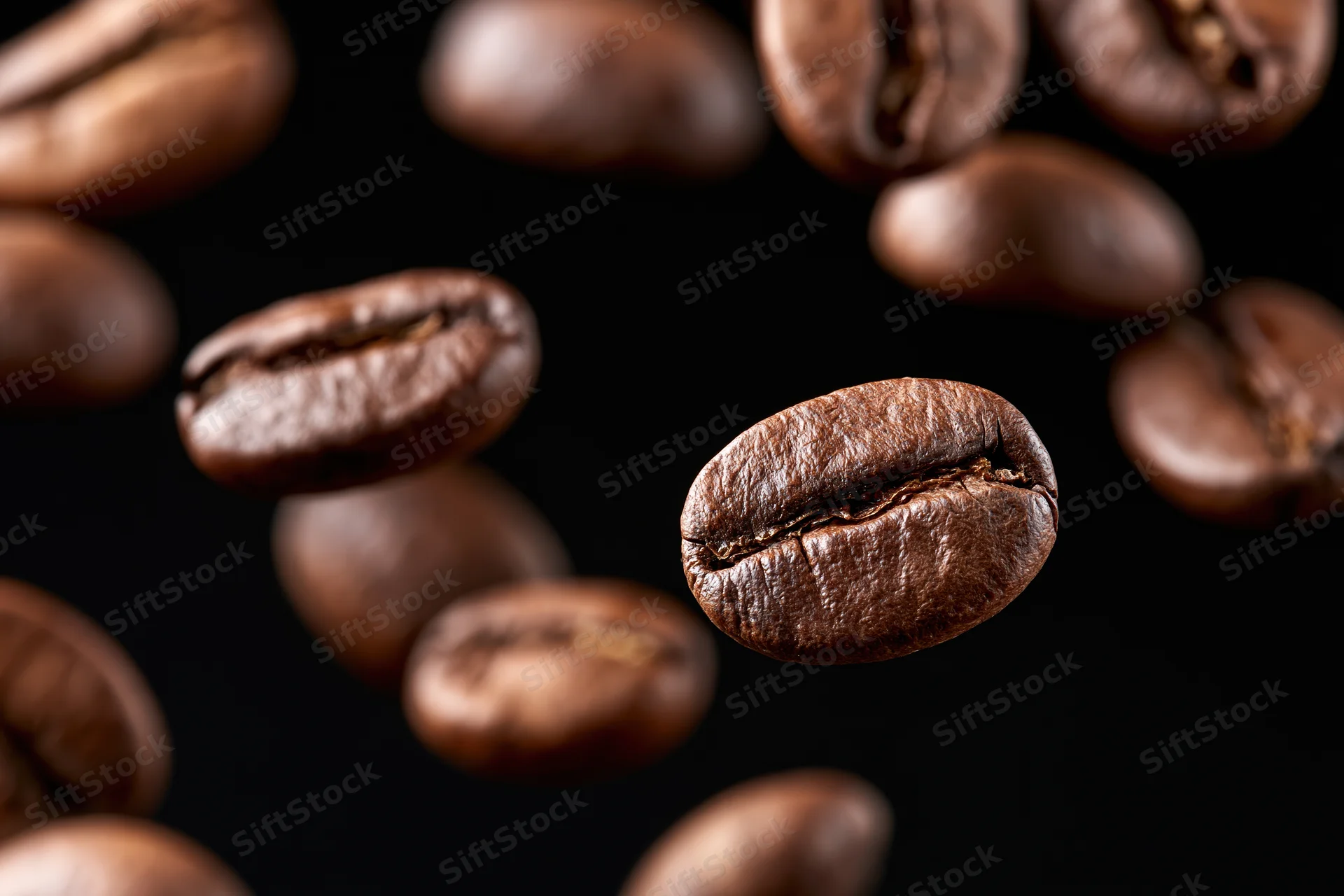 Roasted coffee beans suspended mid-fall against a pure black background