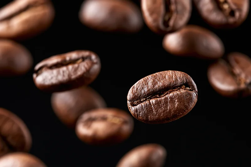 Roasted coffee beans suspended mid-fall against a pure black background