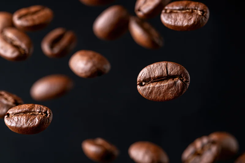 Roasted coffee beans suspended mid-fall against a pure black background
