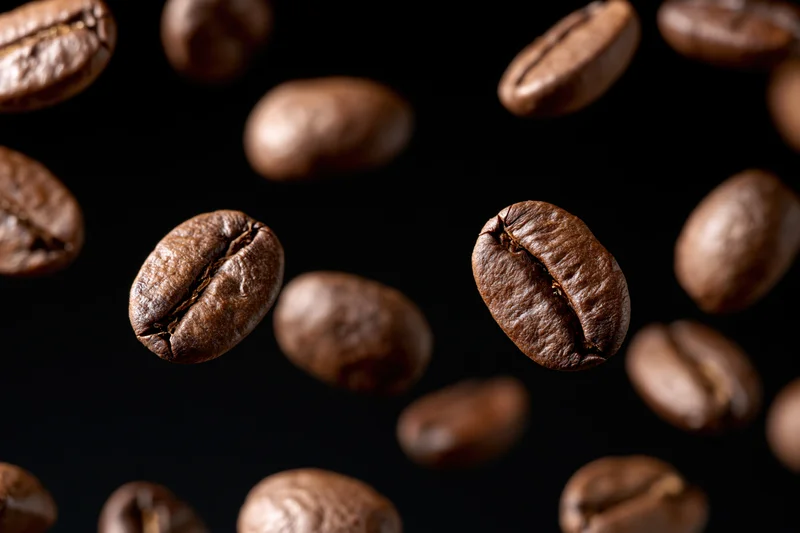 Roasted coffee beans suspended mid-fall against a pure black background