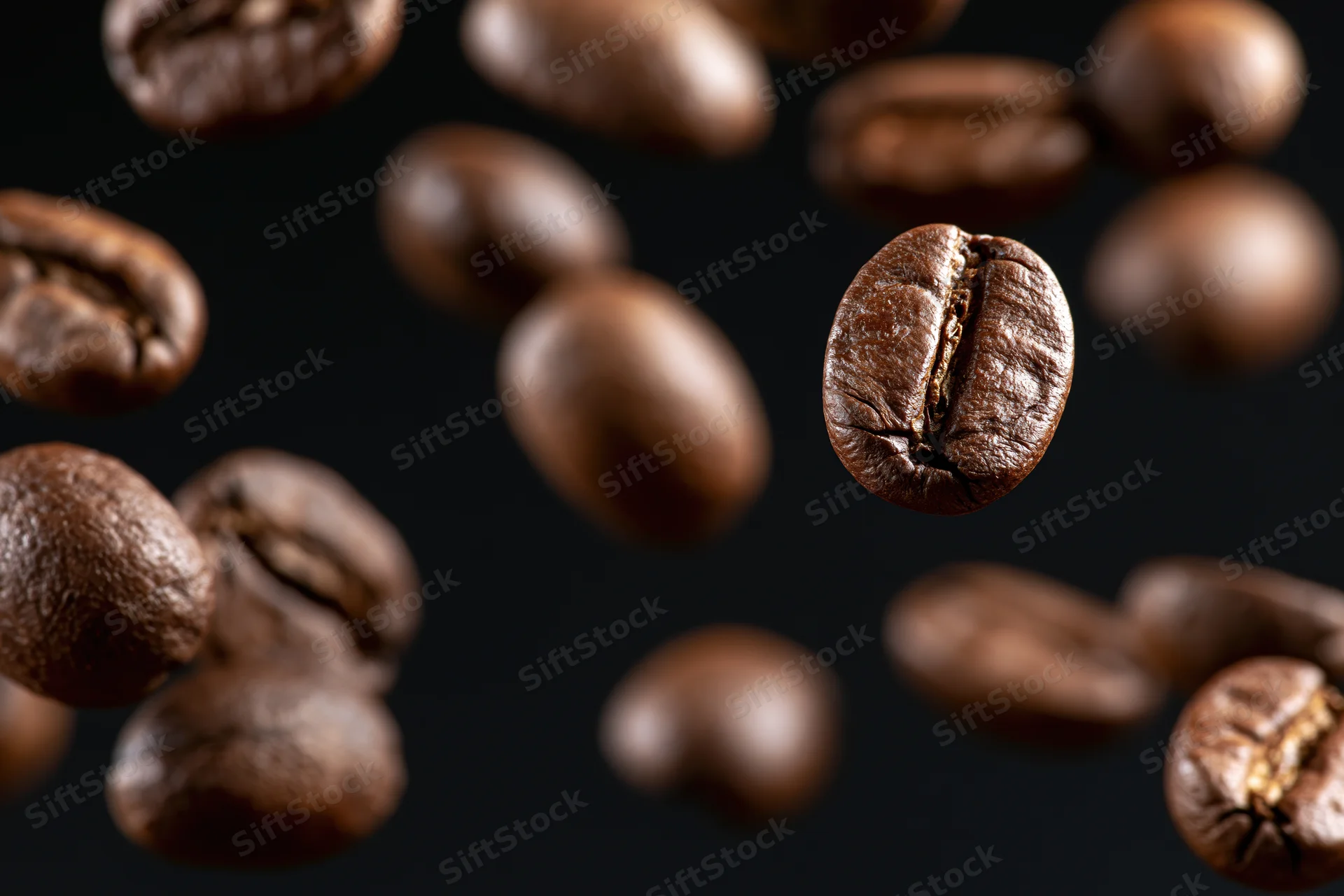 Roasted coffee beans suspended mid-fall against a pure black background
