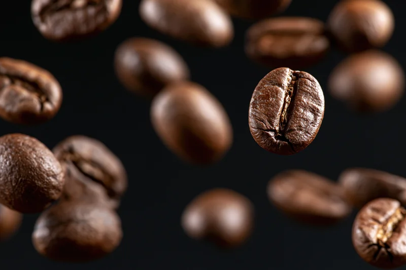 Roasted coffee beans suspended mid-fall against a pure black background