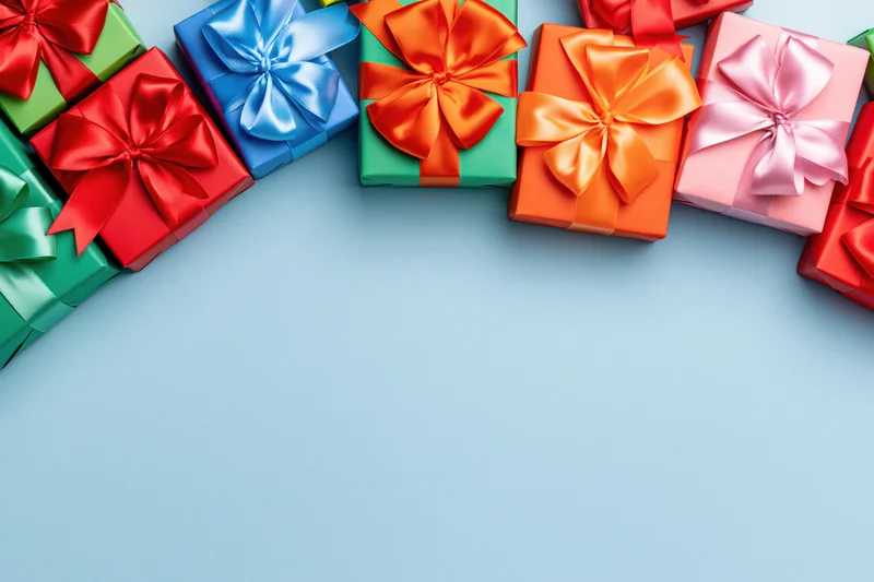 Colorful wrapped gift boxes with satin ribbon bows arranged along the top edge of a light blue surface