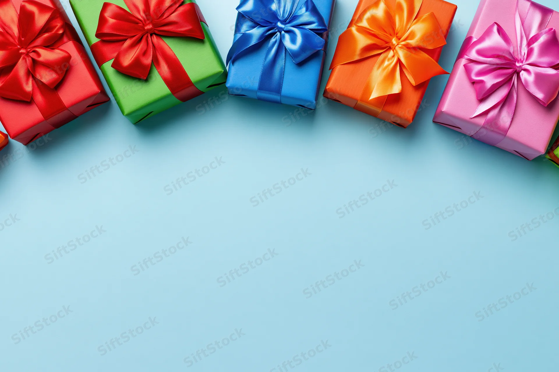 Row of colorful wrapped gift boxes with satin ribbon bows arranged along top edge of light blue surface