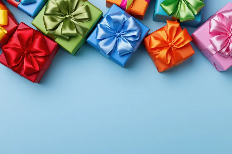 Colorful wrapped gift boxes with satin ribbon bows arranged along the top edge of a light blue surface, leaving copyspace below
