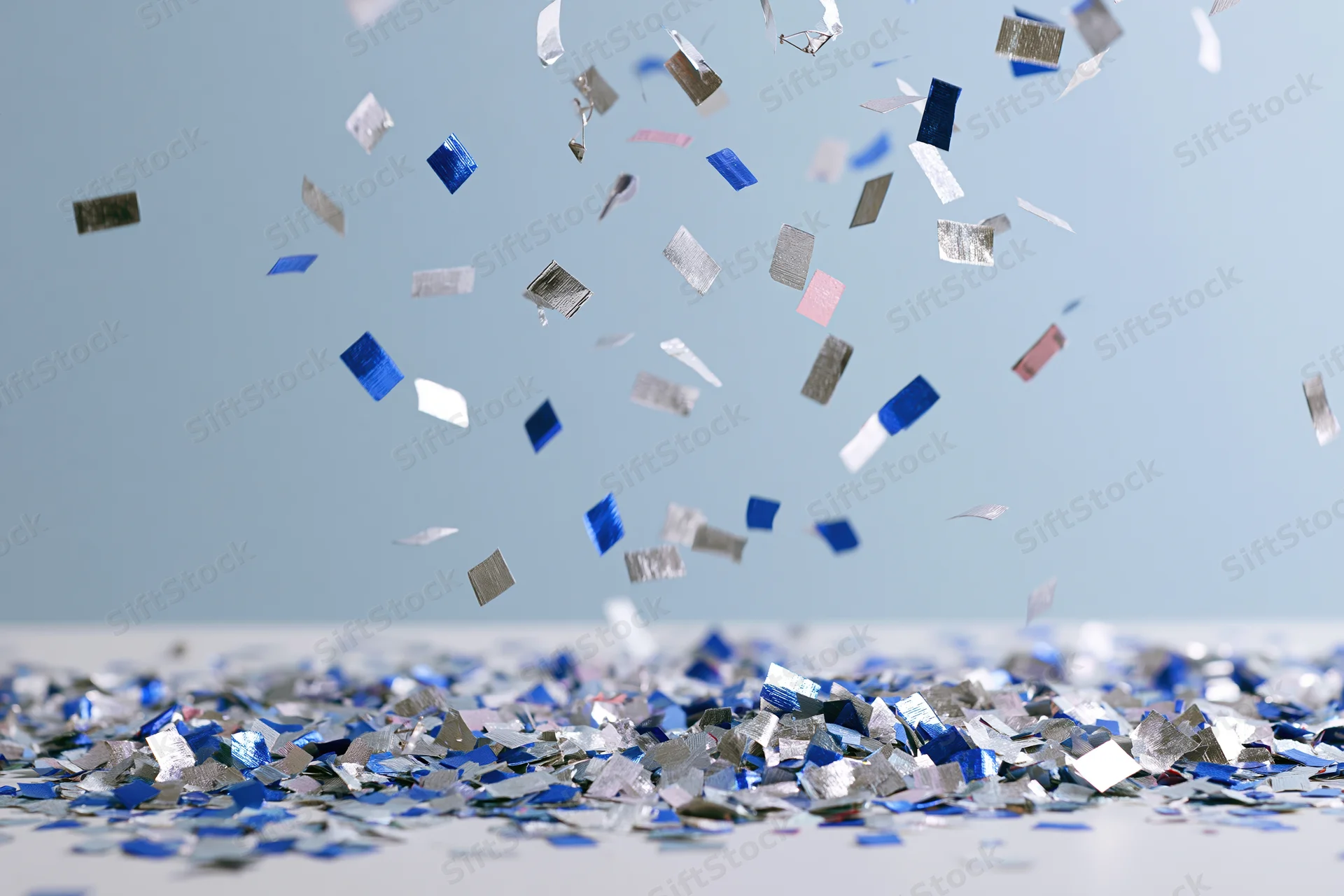 Metallic blue and silver confetti pieces falling and scattered on a light surface