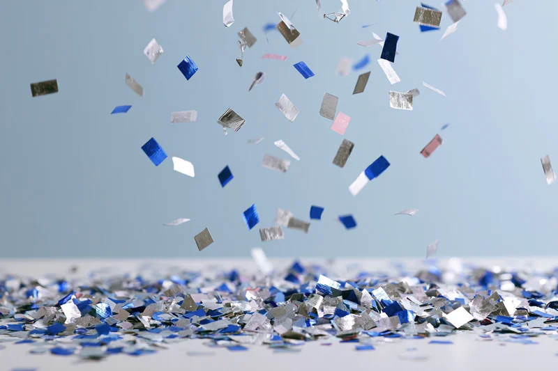 Metallic blue and silver confetti pieces falling and scattered on a light surface