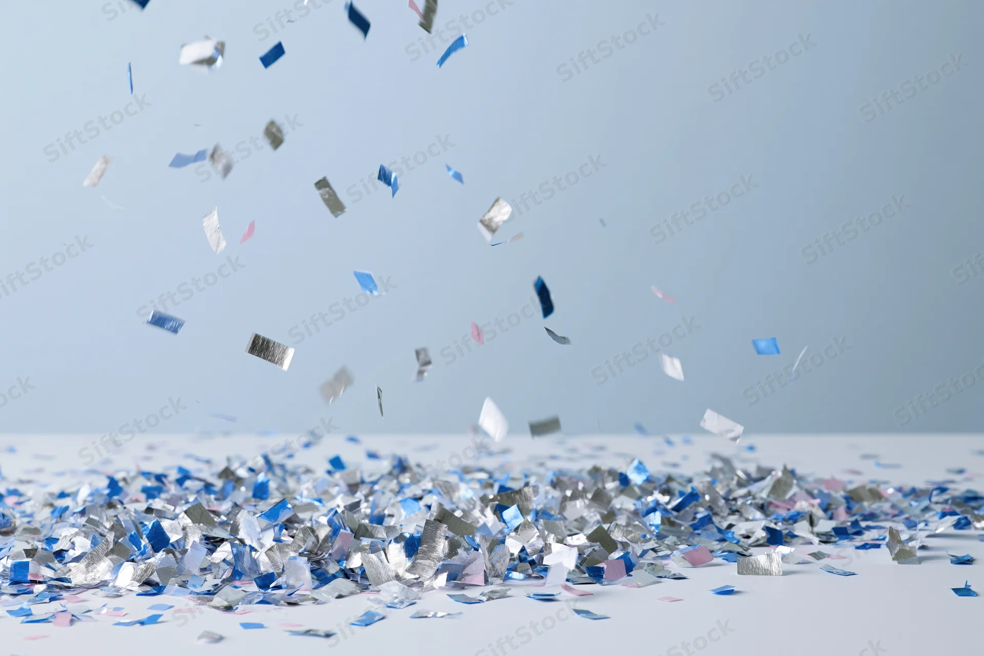 Metallic blue and silver confetti falling and scattered on a white surface