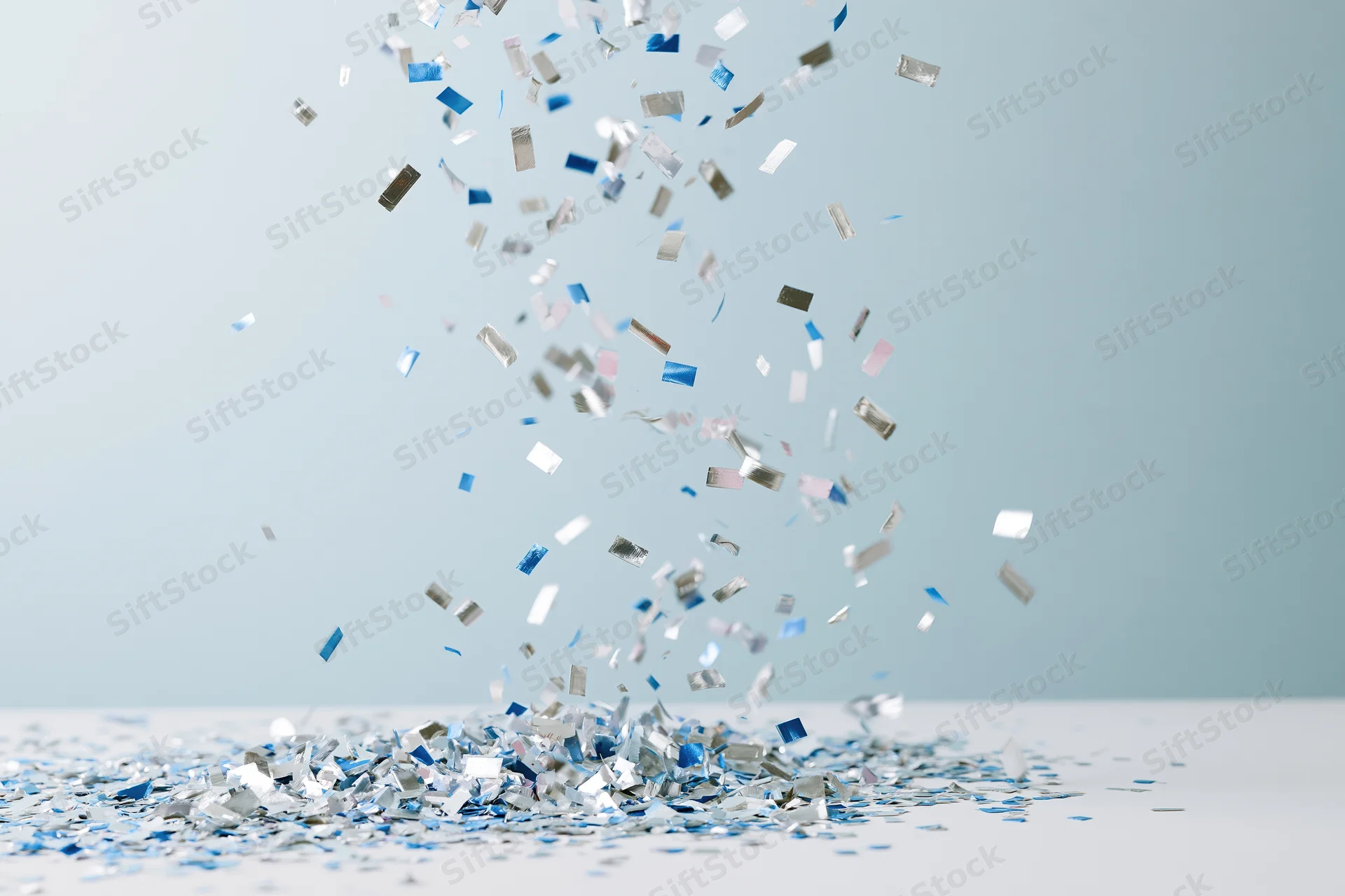 Metallic silver and blue confetti pieces falling and piling on a light surface