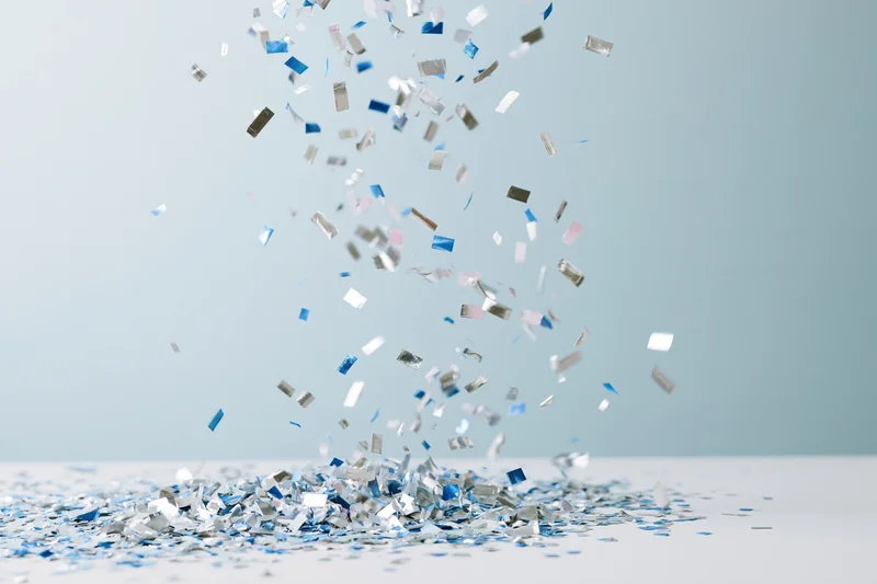 Metallic silver and blue confetti pieces falling and piling on a light surface