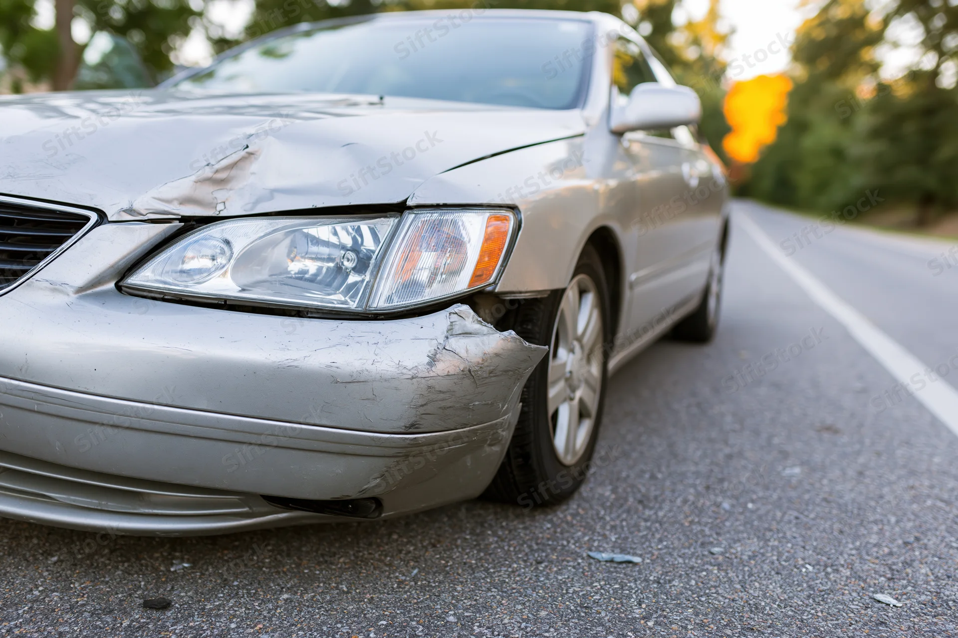 Silver sedan with crumpled front end resting on roadside asphalt