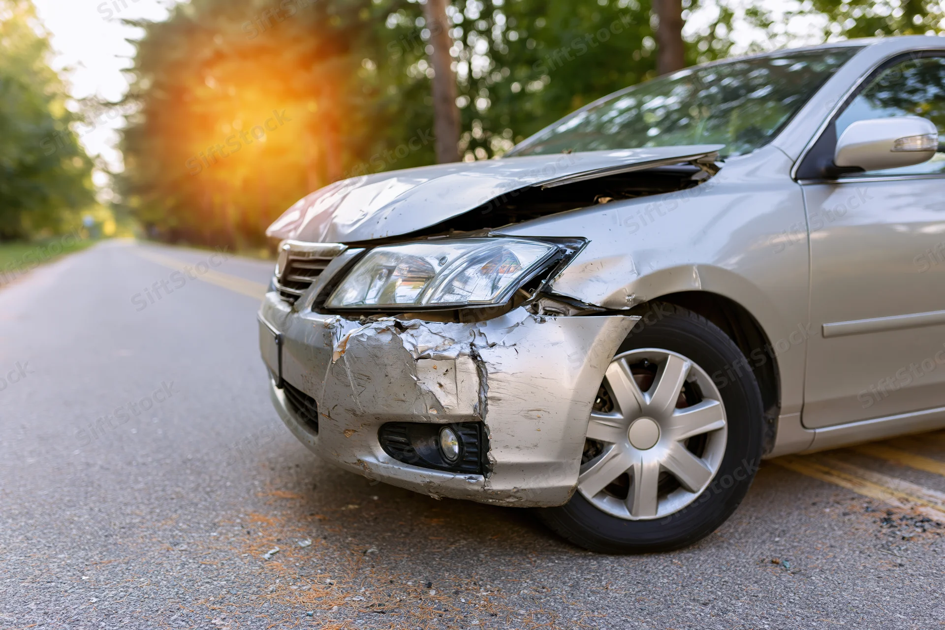 Silver sedan with crumpled front end resting on rural road at daytime