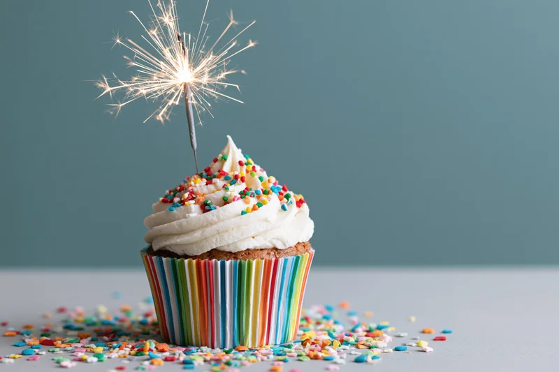 Single birthday cupcake with lit sparkler and colorful sprinkles on a table
