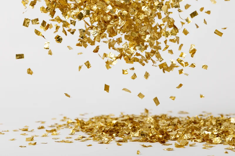 Gold foil confetti falling and scattering on a white surface
