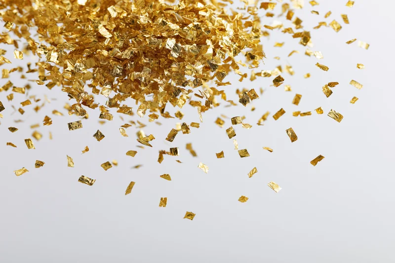 Gold foil confetti pieces falling and scattering against a light background
