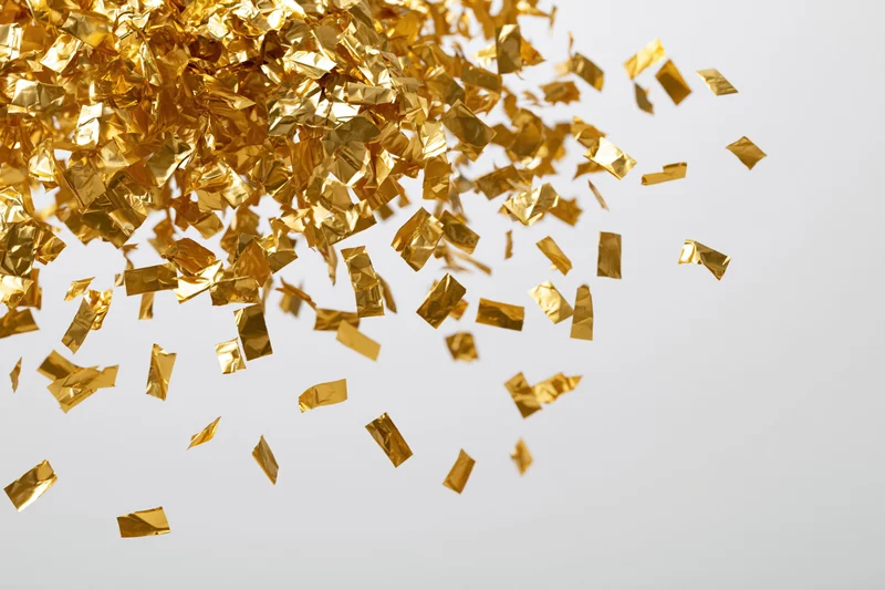 Gold foil confetti falling and scattering across a white background with copyspace on the right