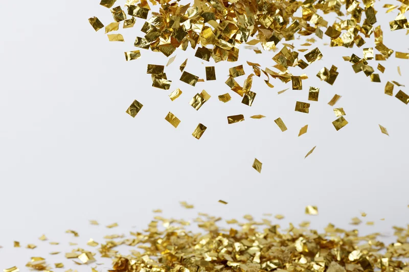 Gold foil confetti falling and scattering on a white surface with copyspace