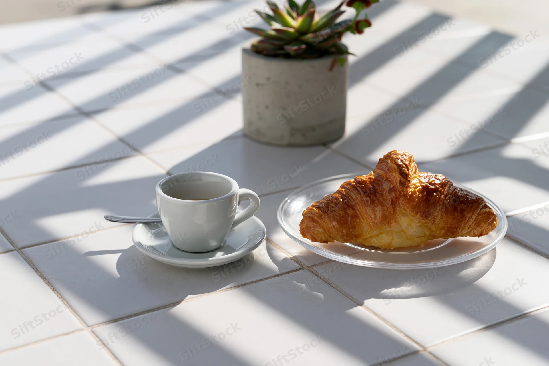 Croissant and espresso cup on a tiled table with sunlight and shadows