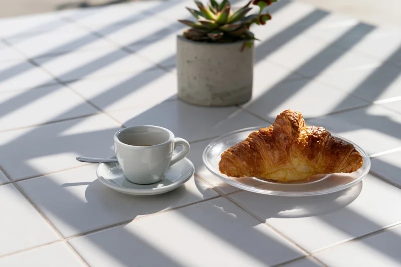 Croissant and espresso cup on a tiled table with sunlight and shadows