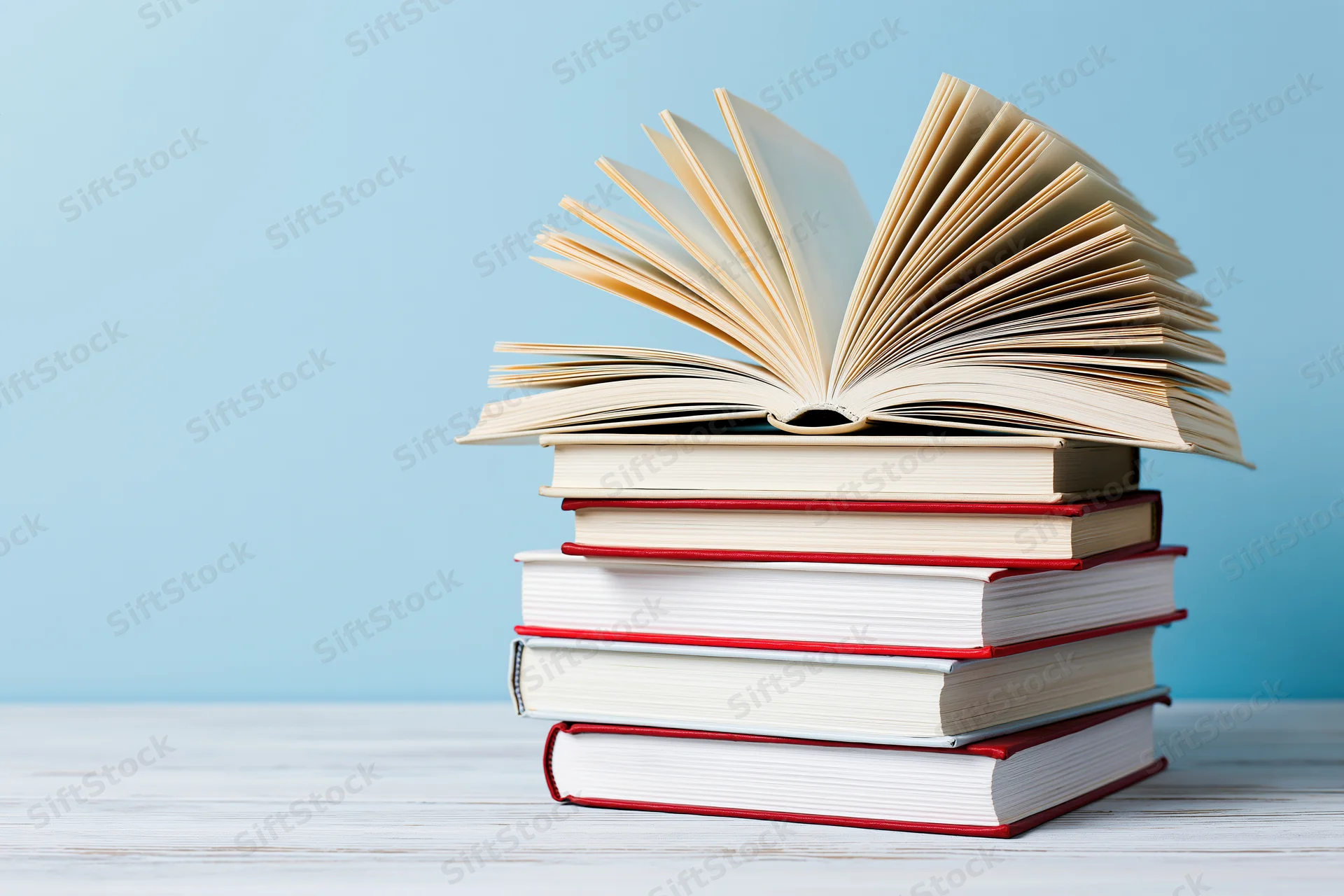 Stack of hardcover books with one open on top on a white wooden surface