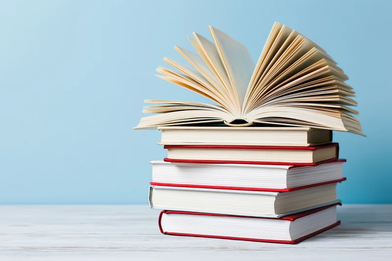 Stack of hardcover books with one open on top on a white wooden surface