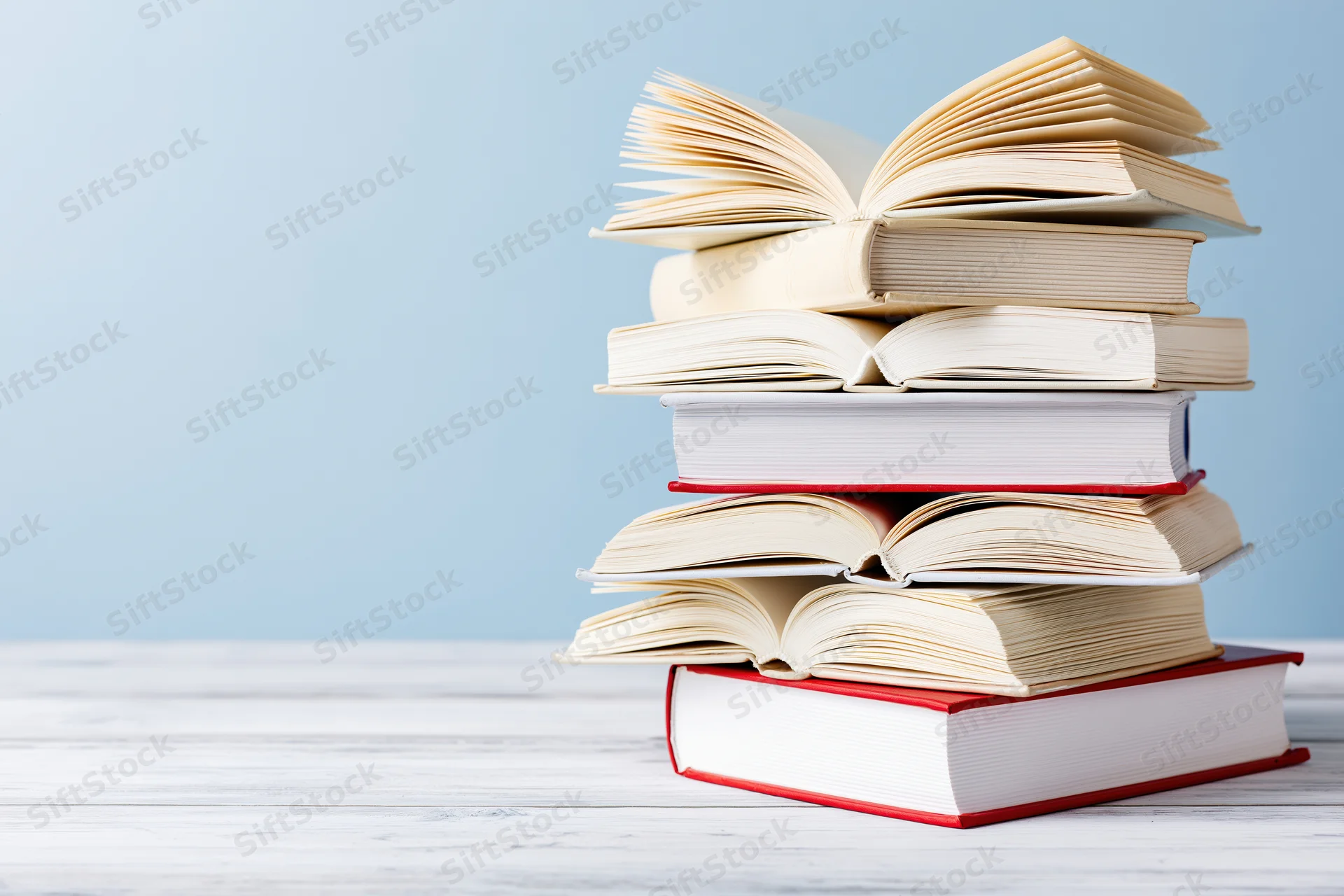 Stack of open hardcover books piled on a white wooden surface