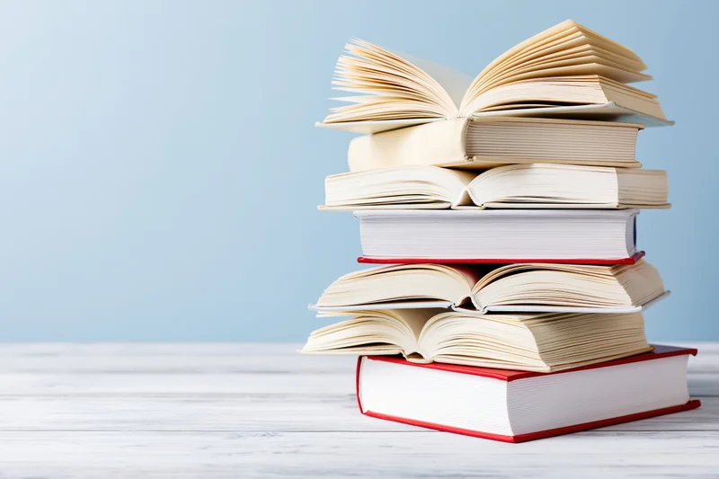 Stack of open hardcover books piled on a white wooden surface