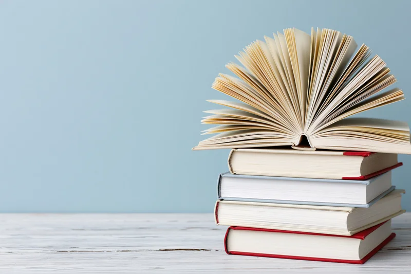 Stack of hardcover books with one open on top on a white wooden surface