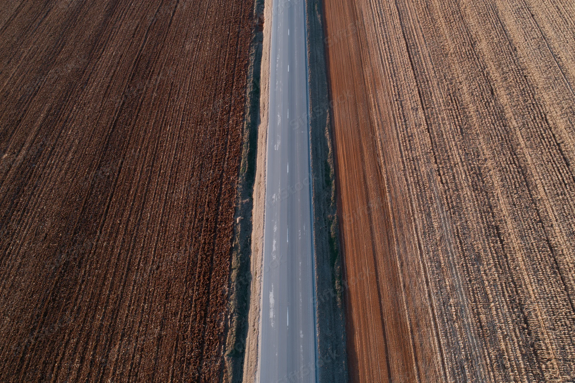Straight asphalt road cutting through plowed agricultural fields from aerial view