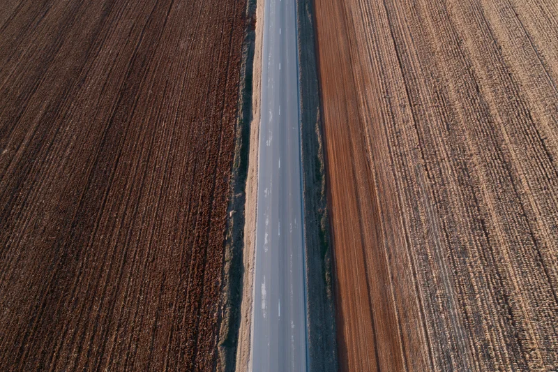 Straight asphalt road cutting through plowed agricultural fields from aerial view