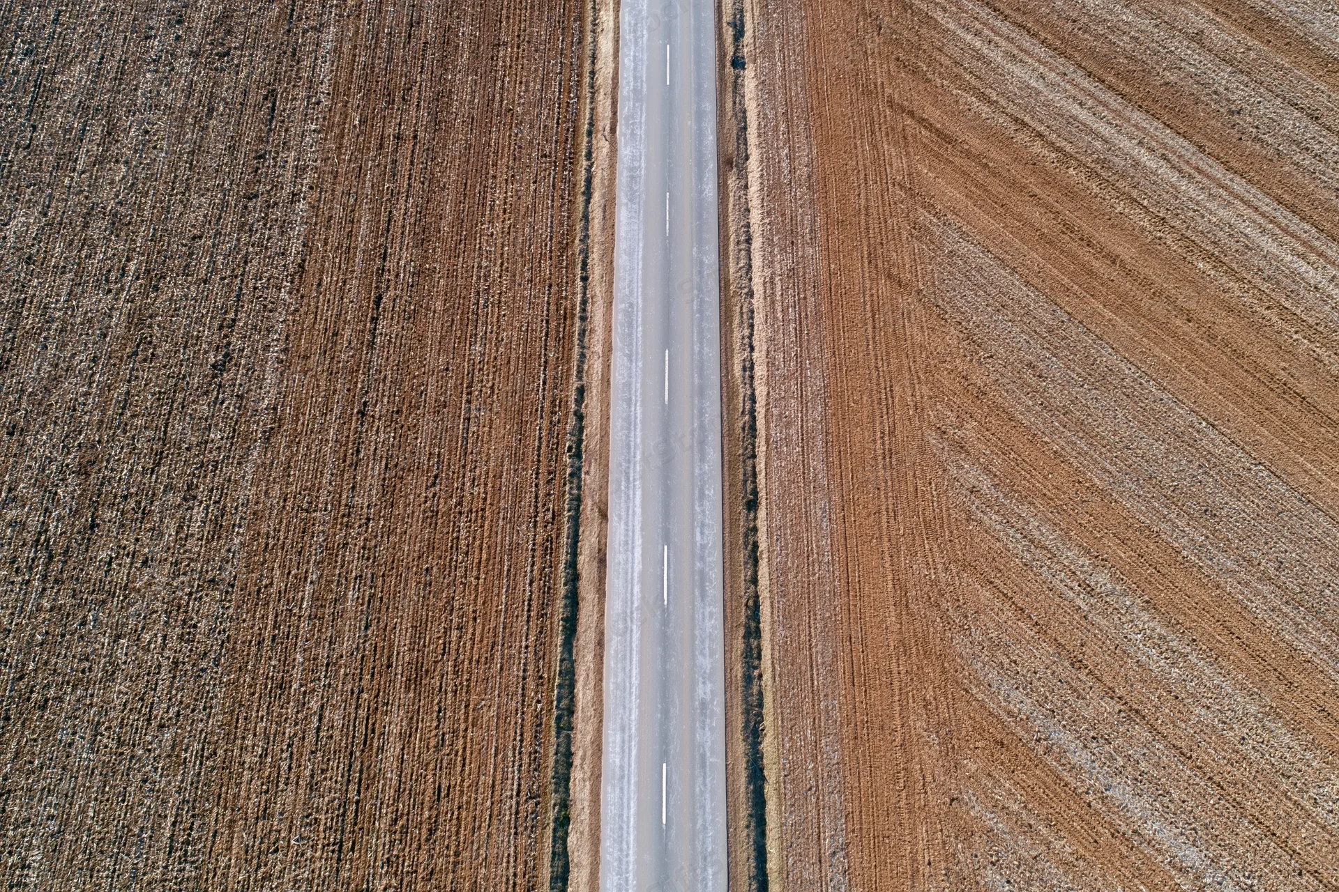 Straight two-lane asphalt road cutting through plowed farmland from above
