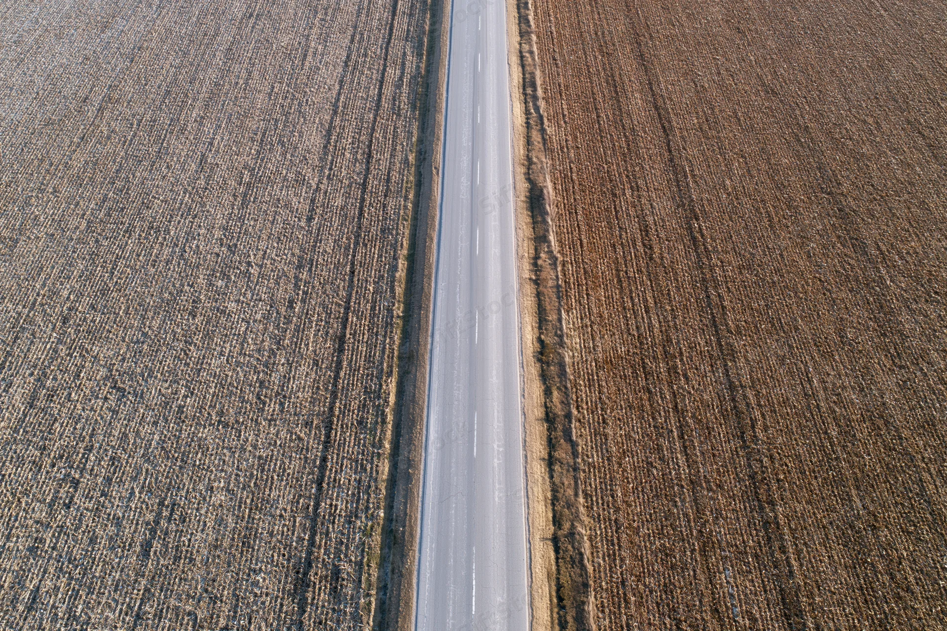Straight two-lane asphalt road cutting through harvested fields from above